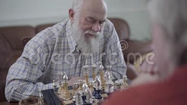 两个老人下棋坐在家里的皮革沙发上。 蓄胡子的人在想<strong>哪个</strong>棋子能动